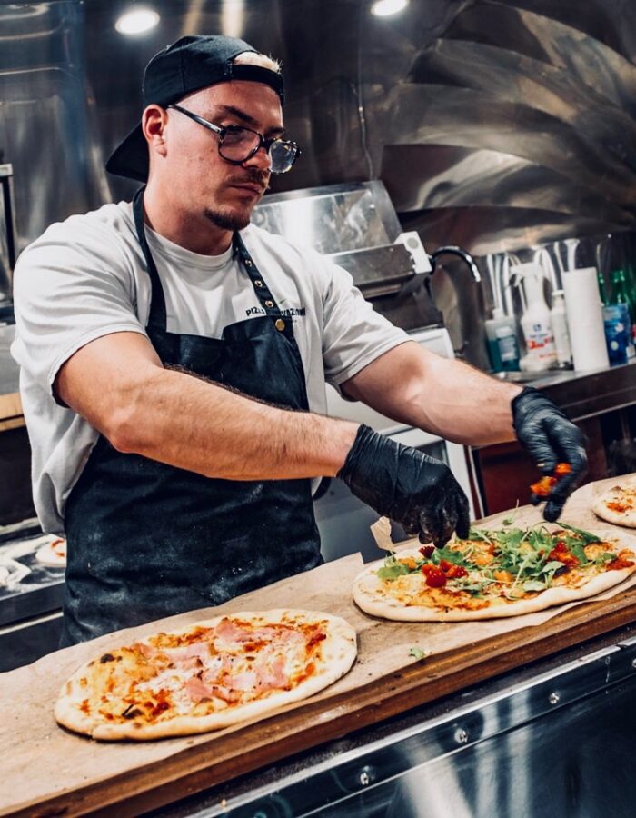 Pizzabäcker belegt frische Pizza mit Rucola und Tomaten im Foodtruck