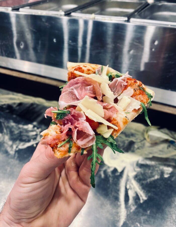 Frisch gebackenes Pizzastück mit Schinken, Rucola und Käse vor dem Pizza-Airstream
