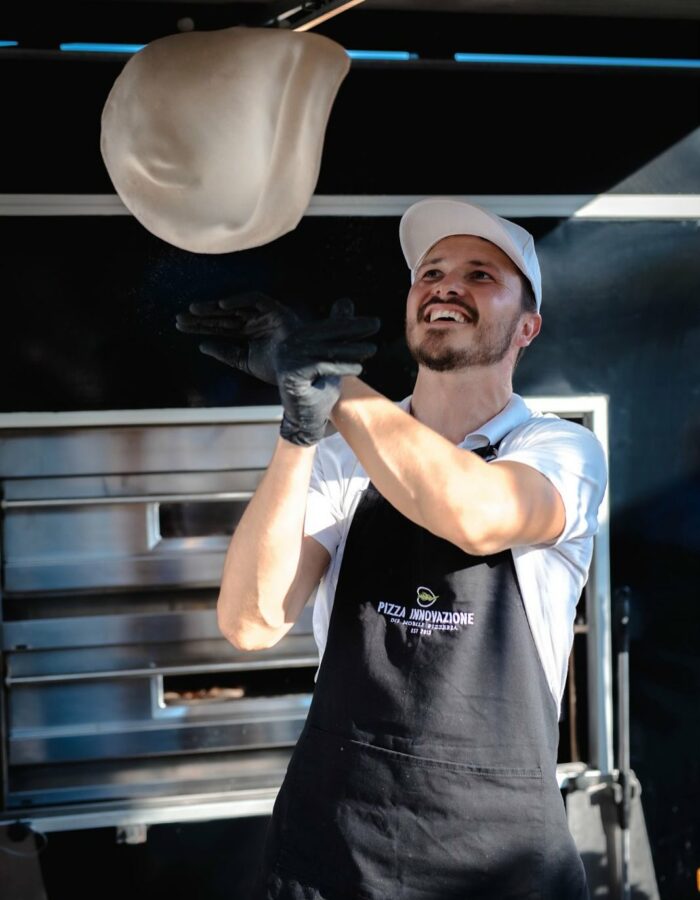 Pizzabäcker wirft frischen Pizzateig beim Live Cooking in die Luft